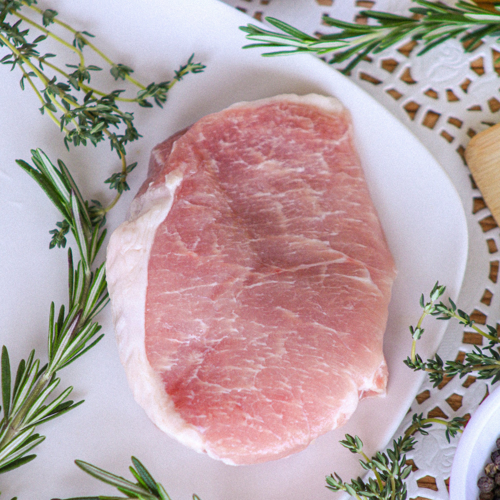 Raw pork chop on a white plate with herbs